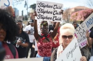 Black woman holds a sign with Stephon Clark's name written on it